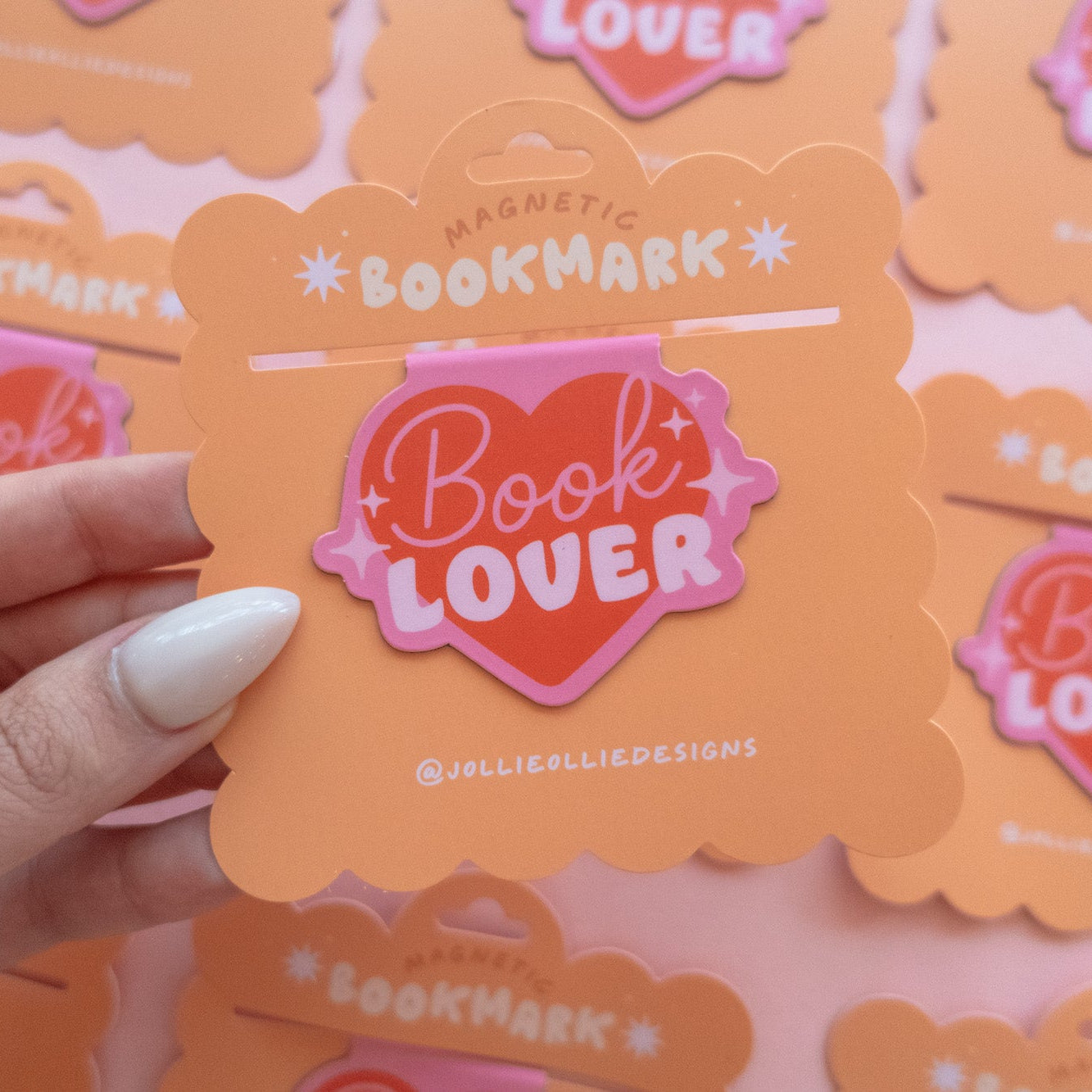 PInk heart 'Book Lover' magnetic bookmark with a hand holding one against a blurred background
