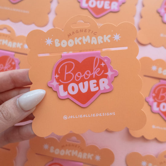 PInk heart 'Book Lover' magnetic bookmark with a hand holding one against a blurred background