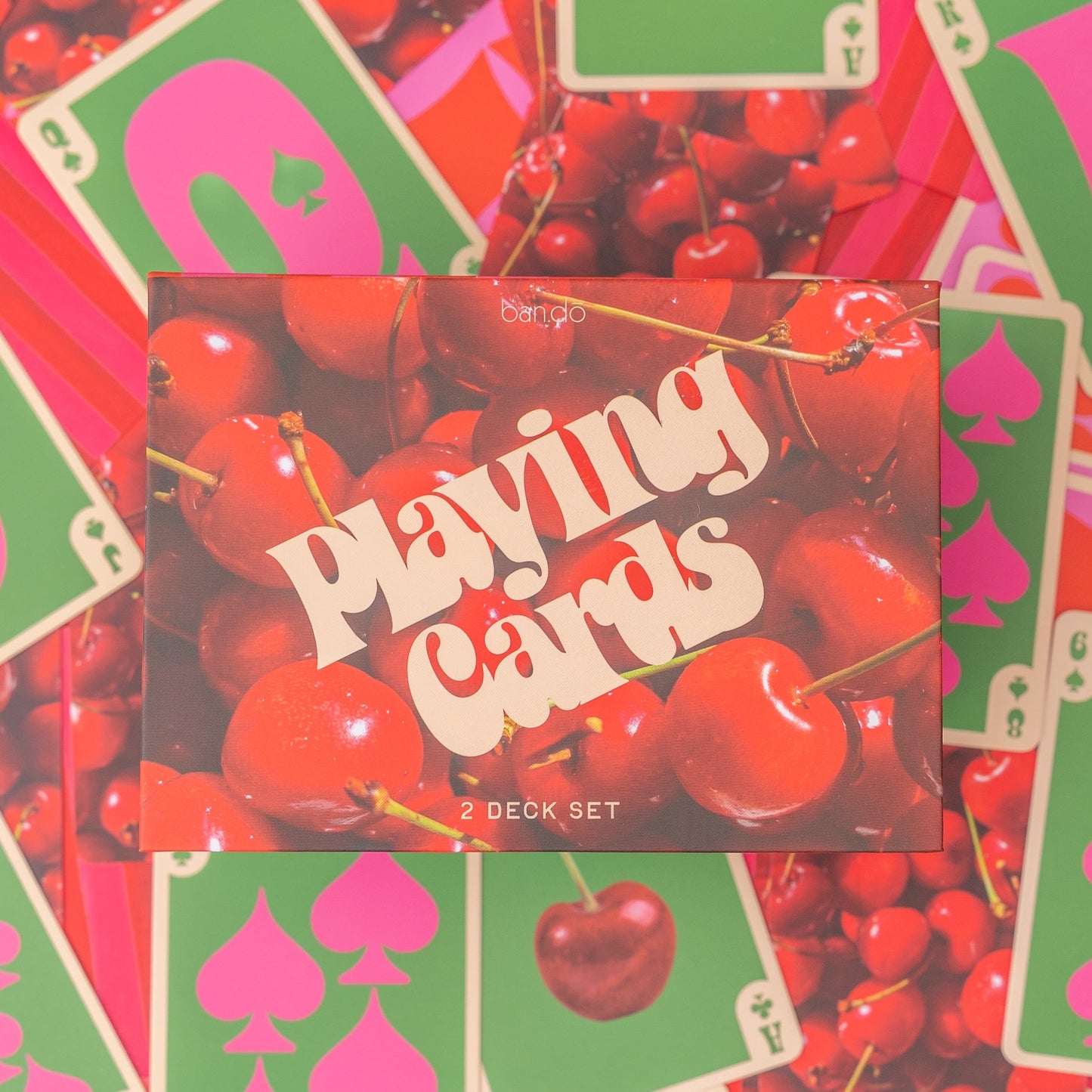 Playing card box with cherry design surrounded by playing cards with red and green designs.