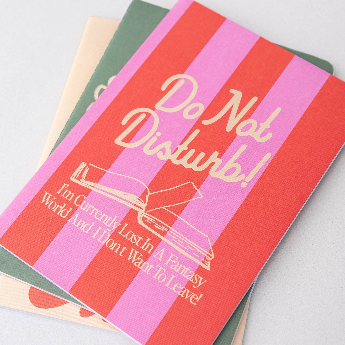 Stack of notebooks with colorful striped covers and humorous text on a light gray background