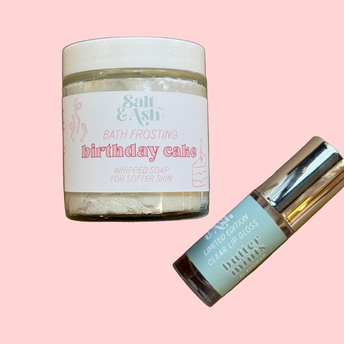 Jar of 'Birthday Cake' bath frosting and a lip gloss on a pink background