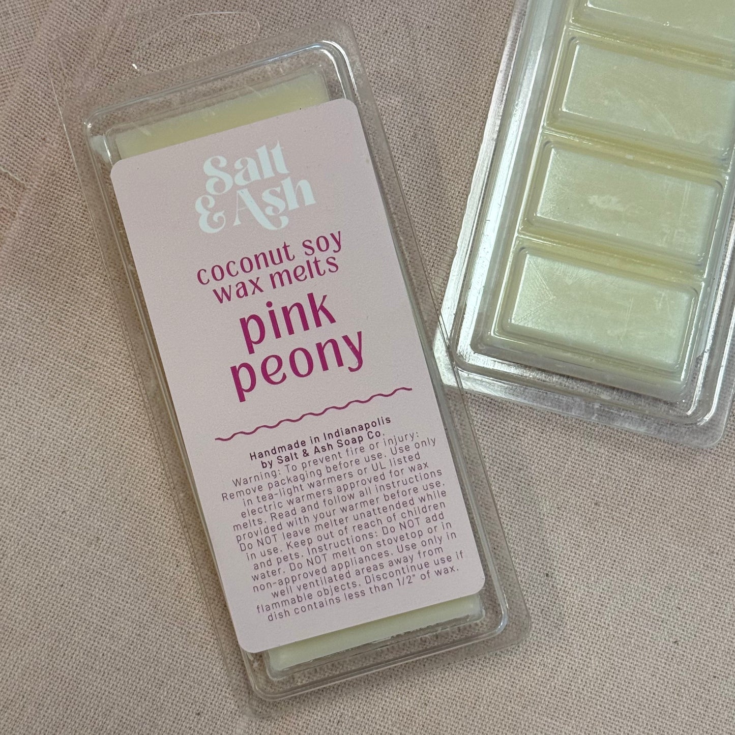 Coconut soy wax melts packaging labeled 'Pink Peony' by Salt & Ash on a beige fabric background.