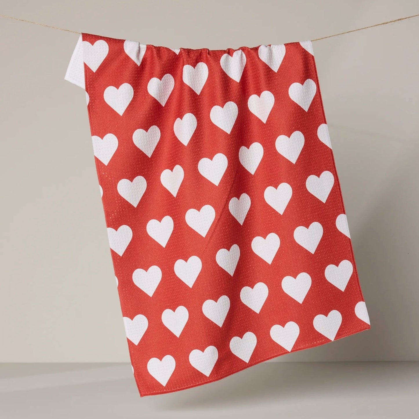 Red towel with white heart pattern hanging on a line against a beige background